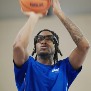 Kuvassa koripalloilija on uuri heitätmässä palloa katseenseurantalasit päässään.